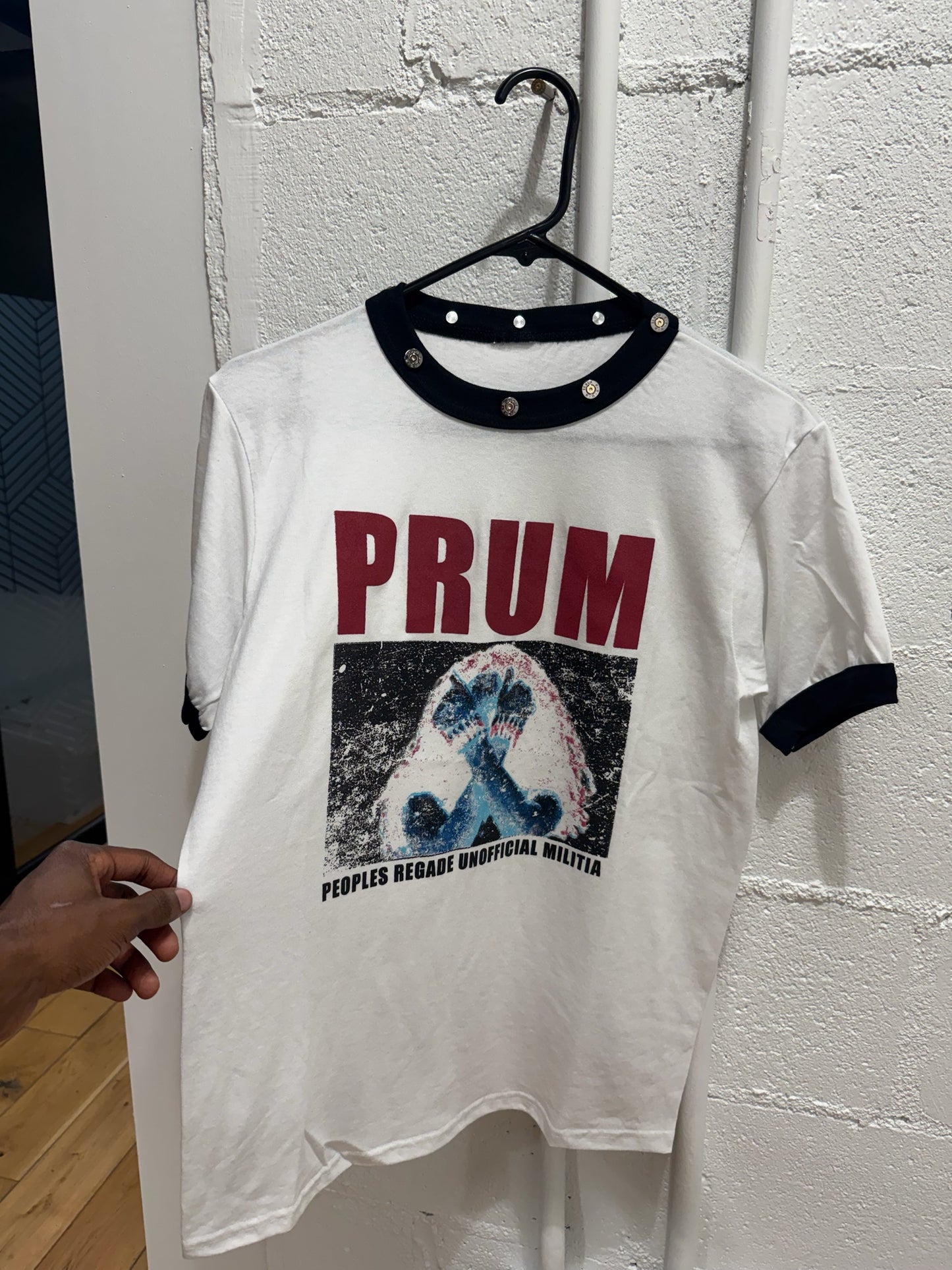 prum.online white cotton ringer t-shirt with black collar, metallic studs, and red and blue graphic print.