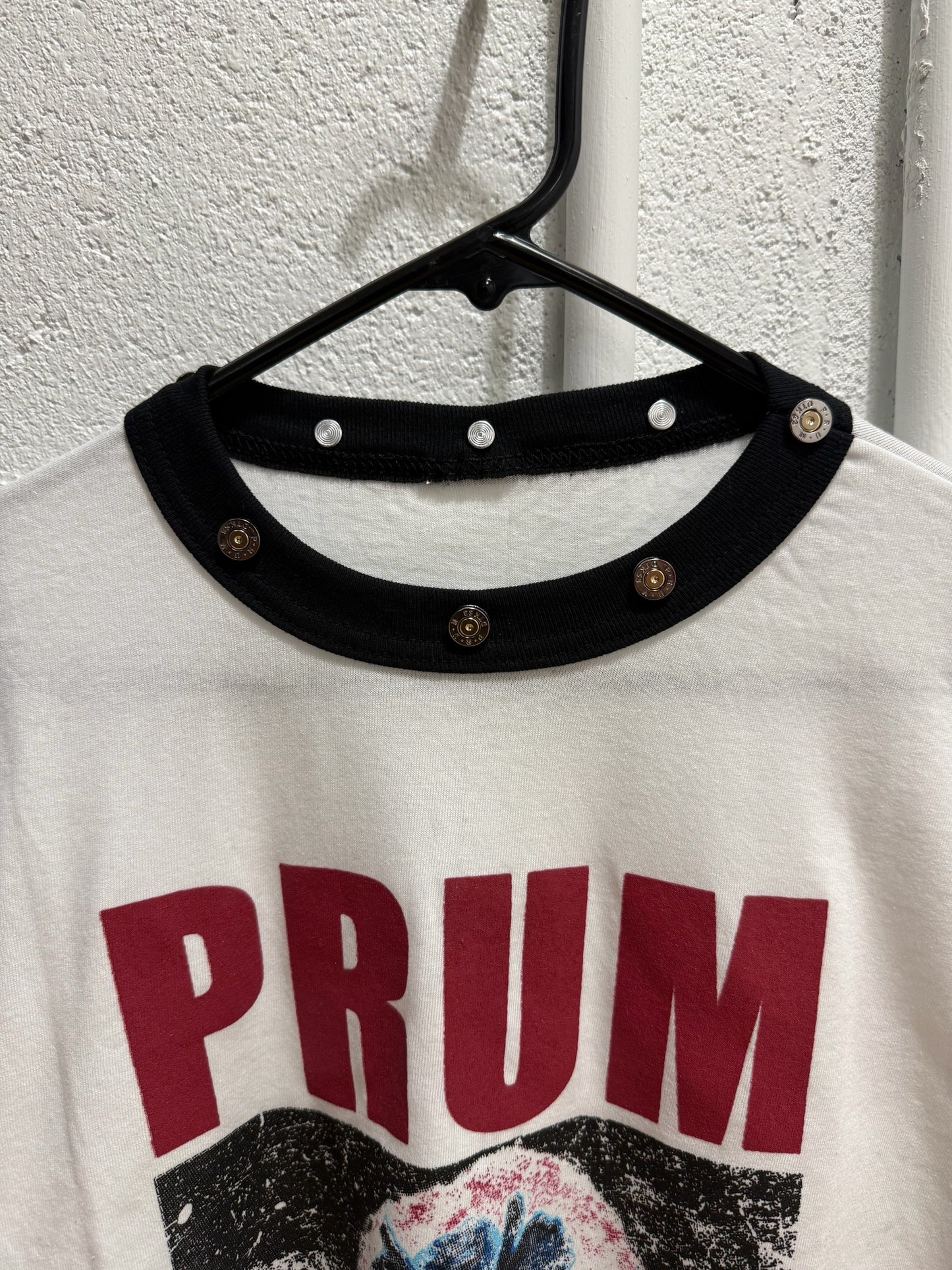 prum.online white ringer t-shirt with black ribbed collar, metallic stud hardware, and red and blue graphic print.