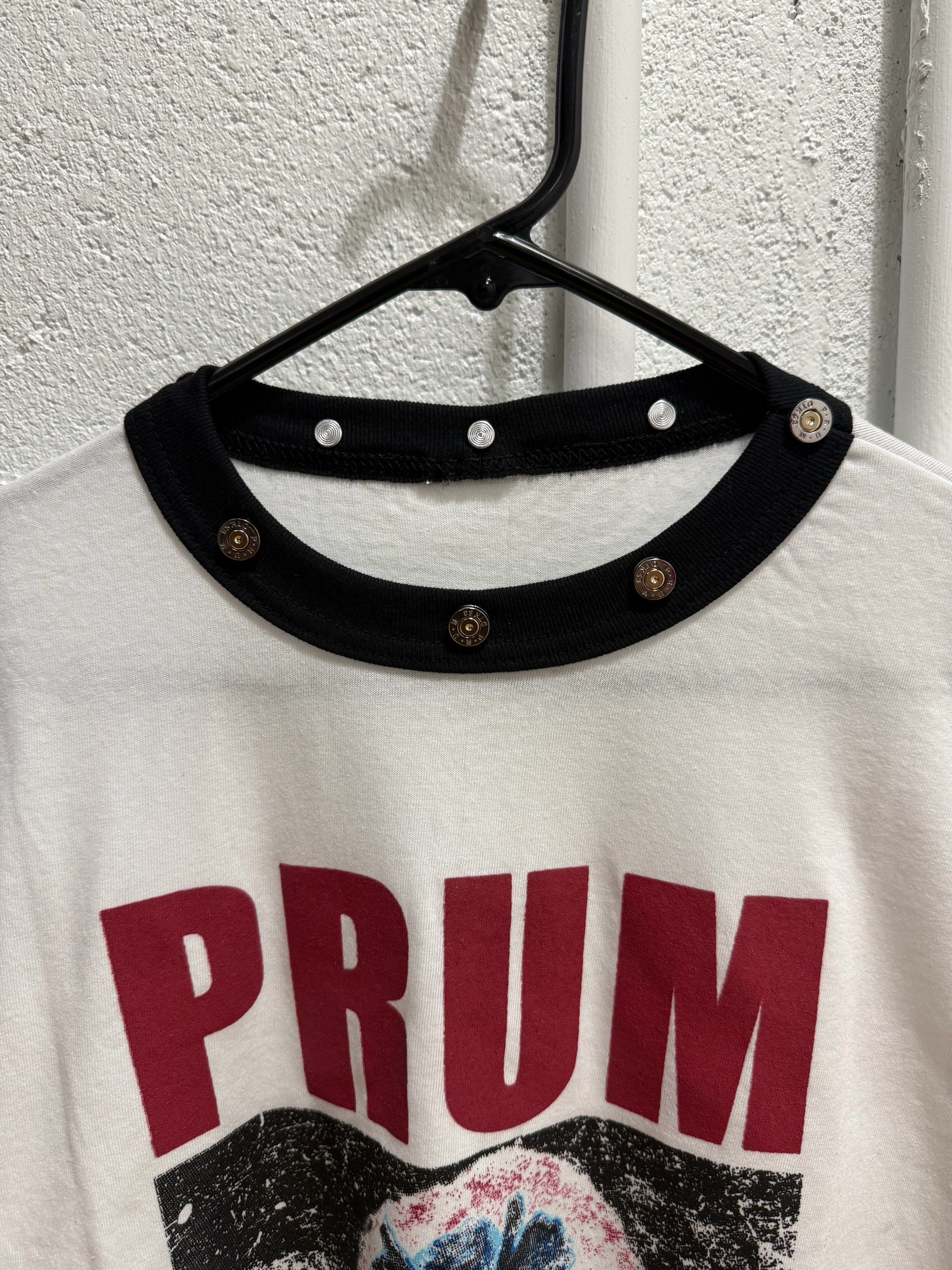 prum.online white ringer t-shirt with black ribbed collar, metallic stud hardware, and red and blue graphic print.